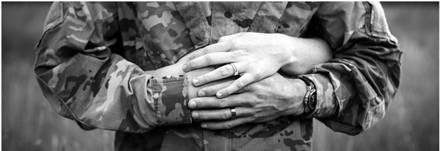 Ma in camouflage holds his hands in front of his chest, with a woman's hand on his from behind
